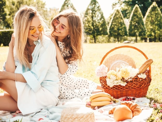A mother and daughter laughing together during a picnic in a park. They are sitting on a blanket with a basket of food, surrounded by trees and flowers.